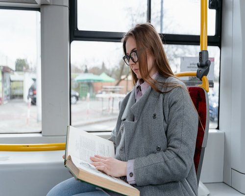 Woman reading a book on a public bus during daytime